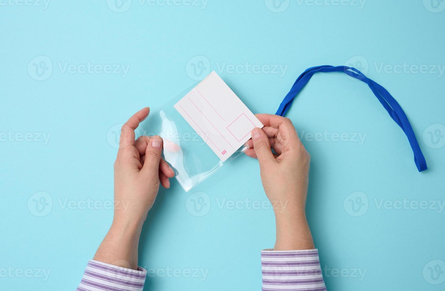 mão feminina segura distintivo de plástico transparente em um cordão azul sobre fundo azul foto