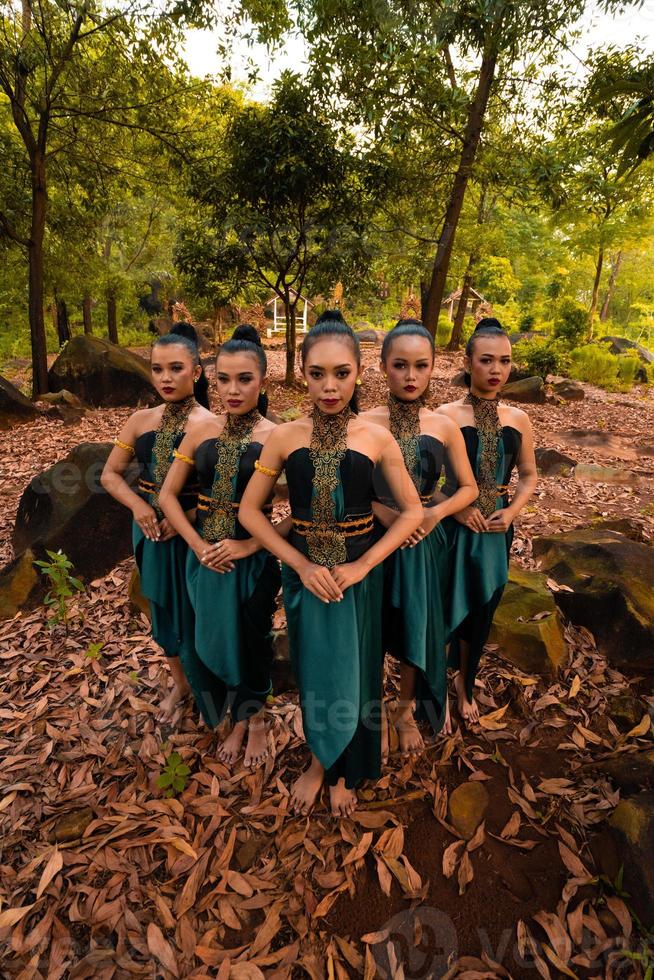 glamour mulheres asiáticas com trajes verdes e maquiagem se alinham na selva com folhas marrons no chão foto