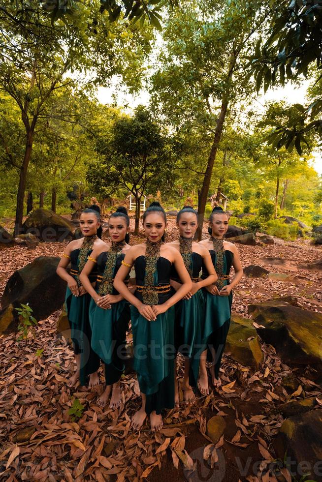 uma foto ampla de uma mulher asiática de pé juntos na floresta enquanto usava uma fantasia de dança verde com folhas mortas