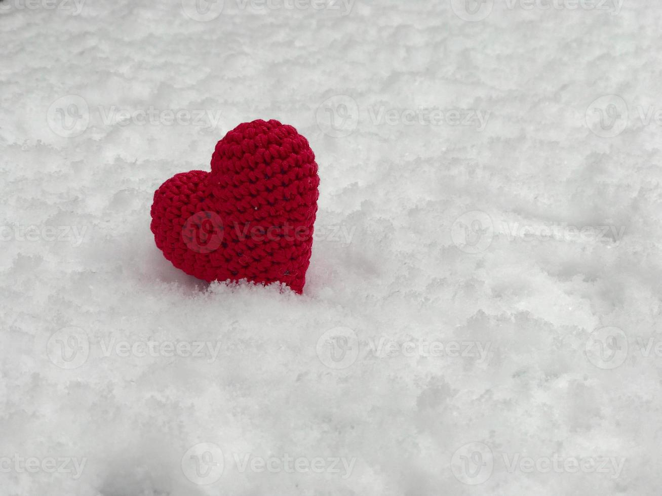 pequeno coração de malha vermelho deitado na neve branca foto