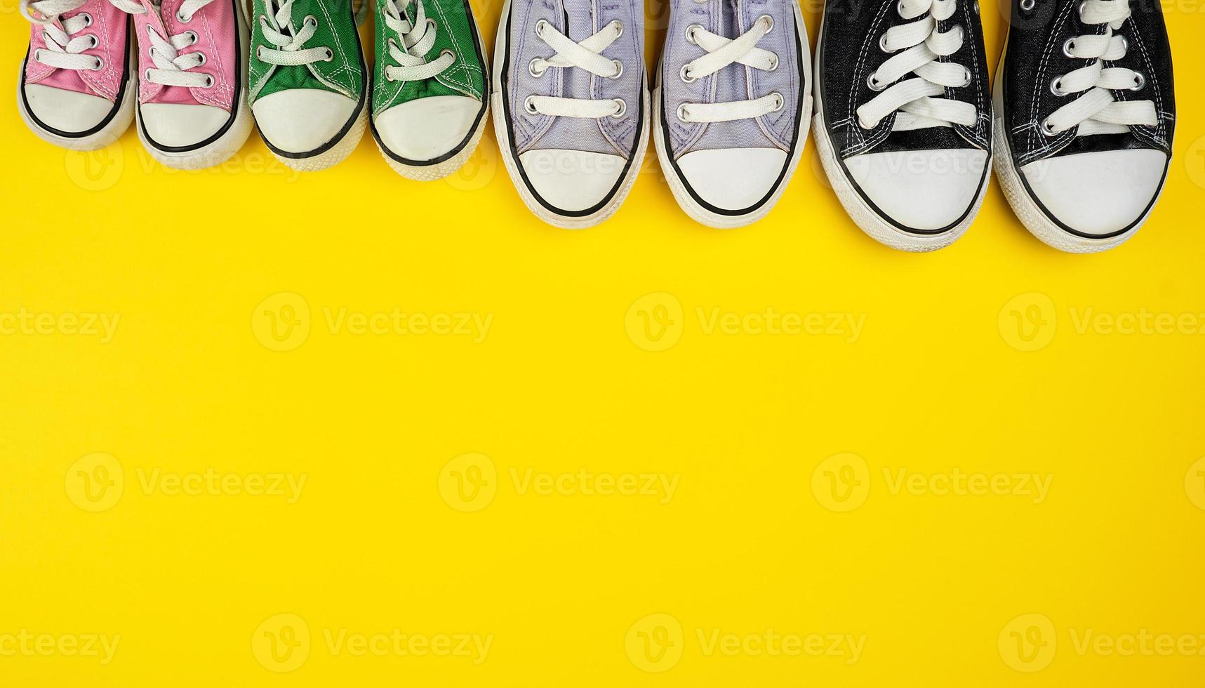 muitos tênis usados têxteis de tamanhos diferentes em um fundo amarelo foto