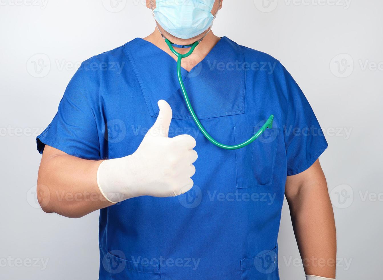 médico masculino em uniforme azul e luvas brancas de látex mostra gesto com a mão direita como foto