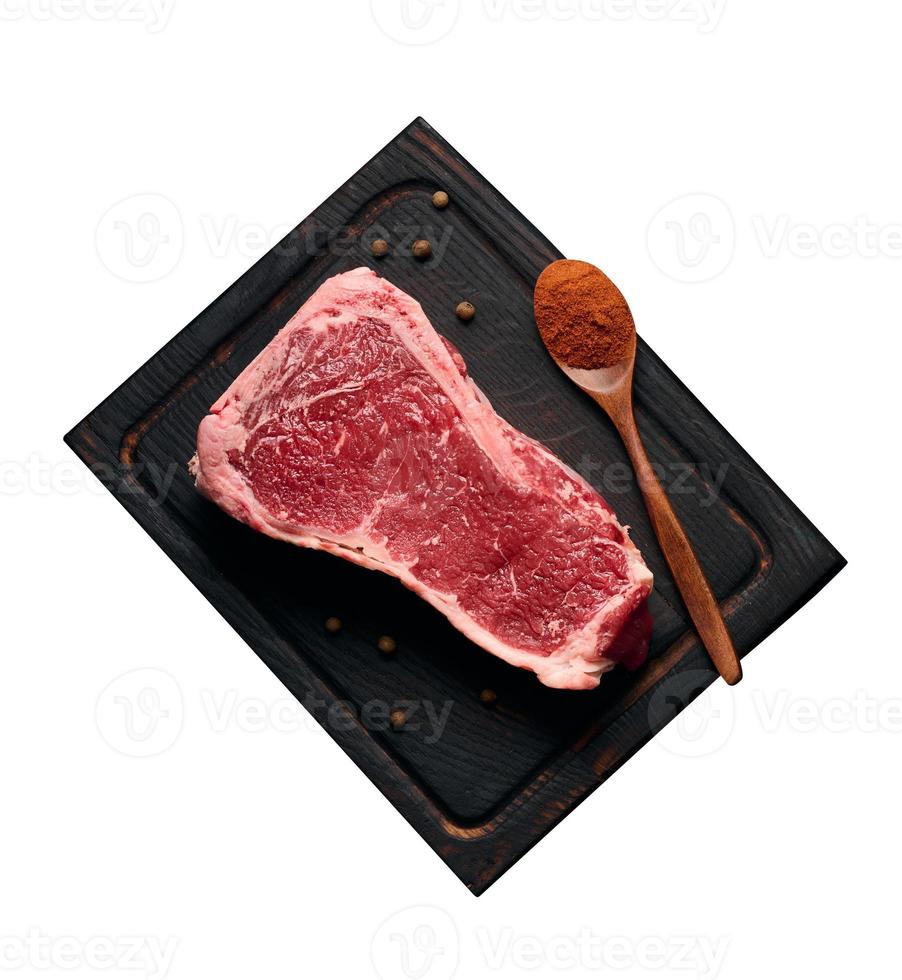 pedaço suculento cru de carne bovina com osso está sobre uma tábua de corte de madeira, especiarias para cozinhar em um fundo preto. lombo de carne nova york foto