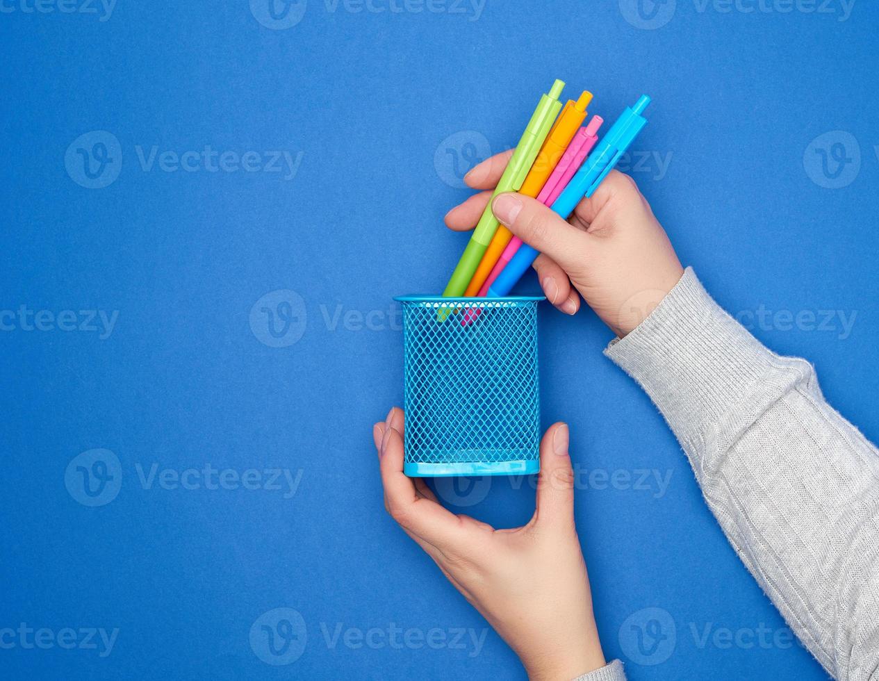 mãos femininas segurando canetas de plástico multicoloridas para desenho e um suporte de papelaria azul metálico foto