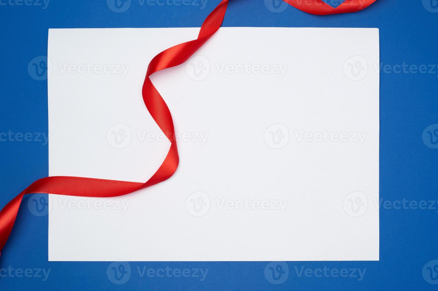 folha de papel branca vazia e fita torcida de seda vermelha em um fundo azul foto