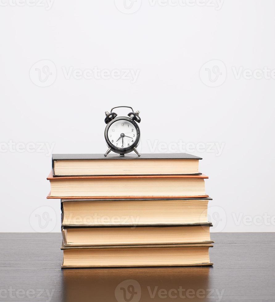 pilha de livros e um despertador preto em cima da mesa foto