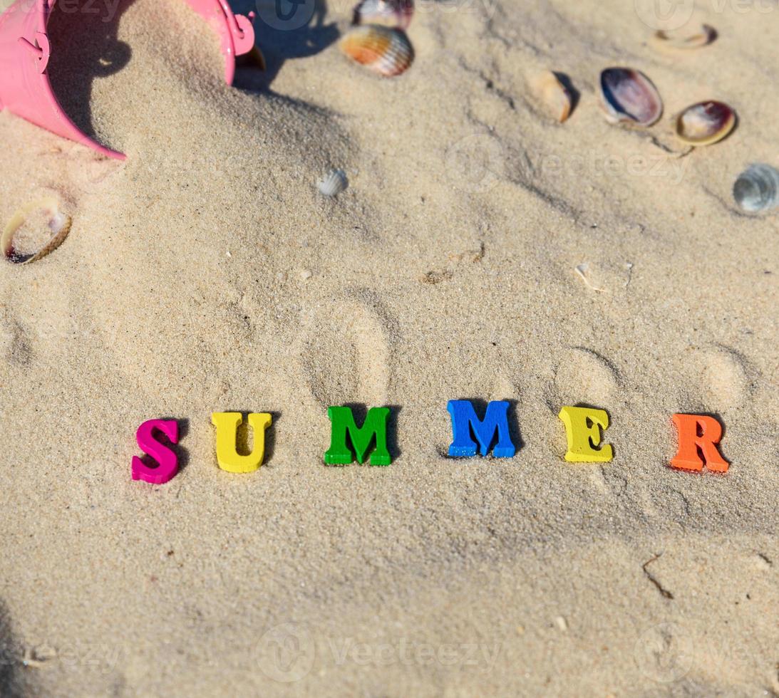 verão de inscrição feito de letras de madeira na areia amarela foto