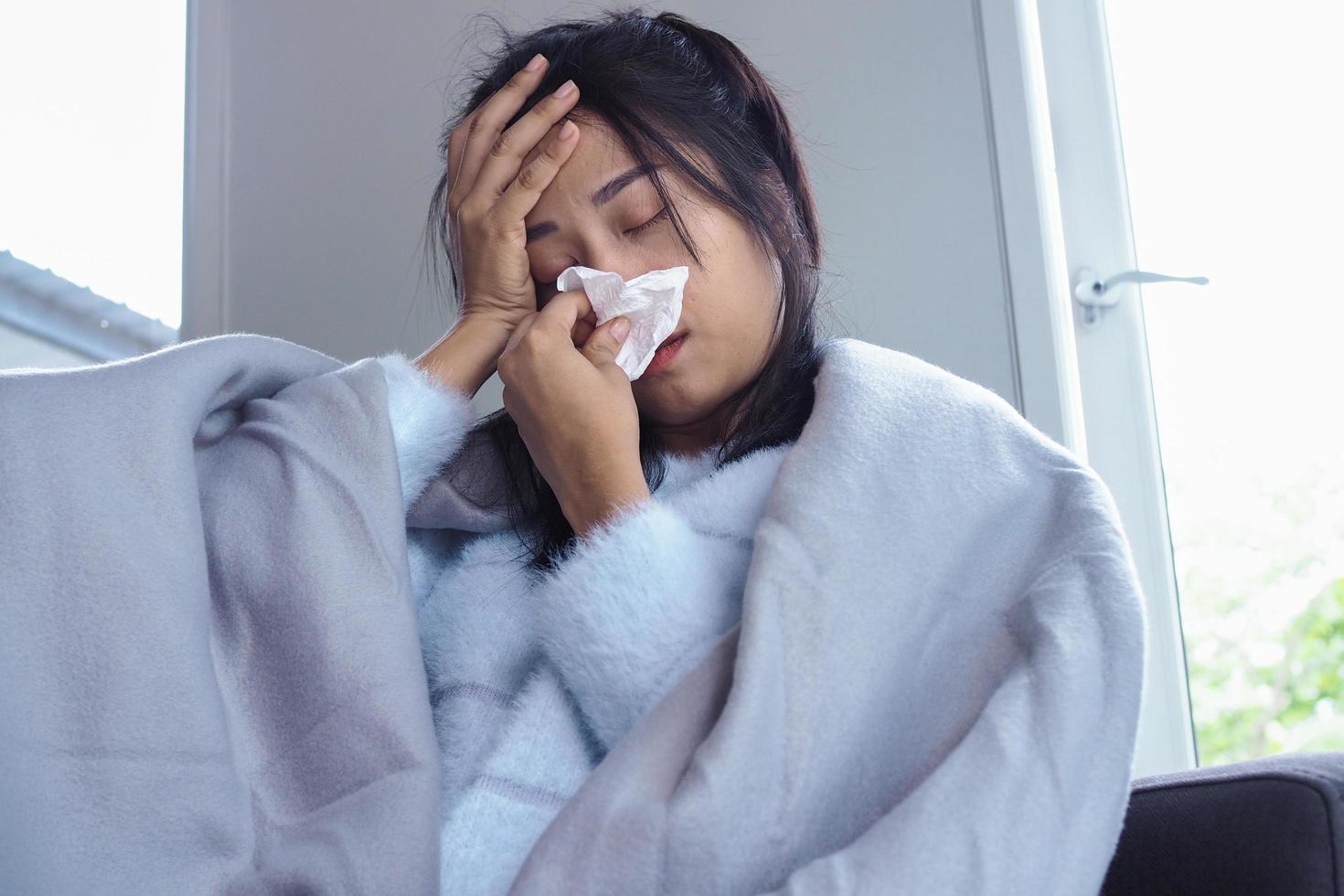 mulher está doente com dor de cabeça, febre alta e gripe, sentada debaixo de um cobertor foto