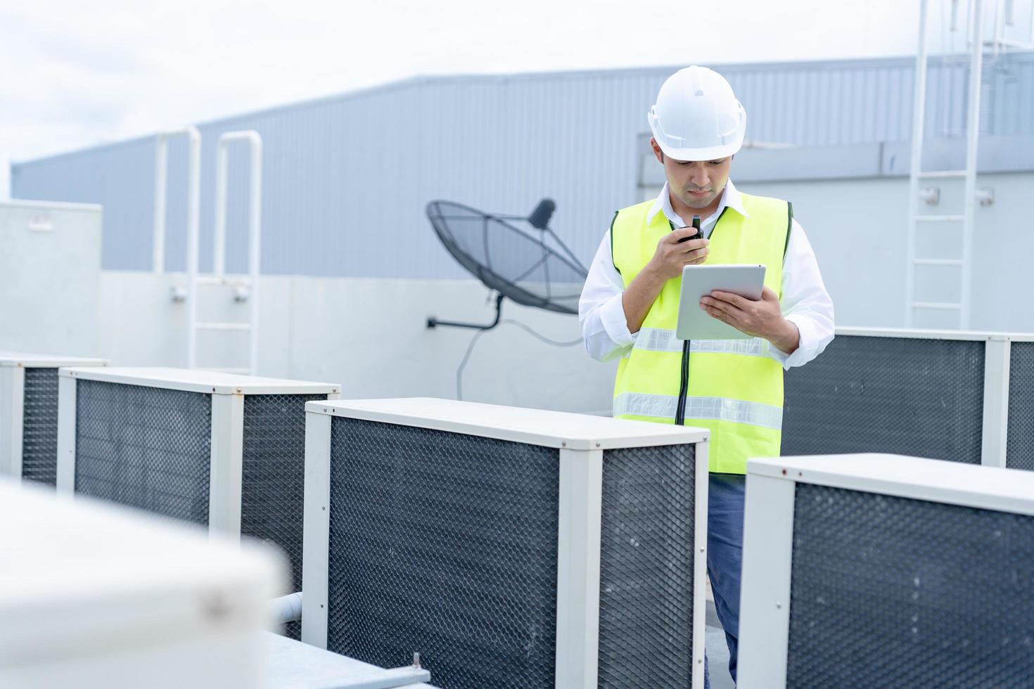 engenheiro de manutenção asiático trabalha no telhado da fábrica. o empreiteiro inspeciona o sistema de compressores e planeja a instalação de sistemas de ar condicionado na construção. tecnologia, verificação on-line. foto