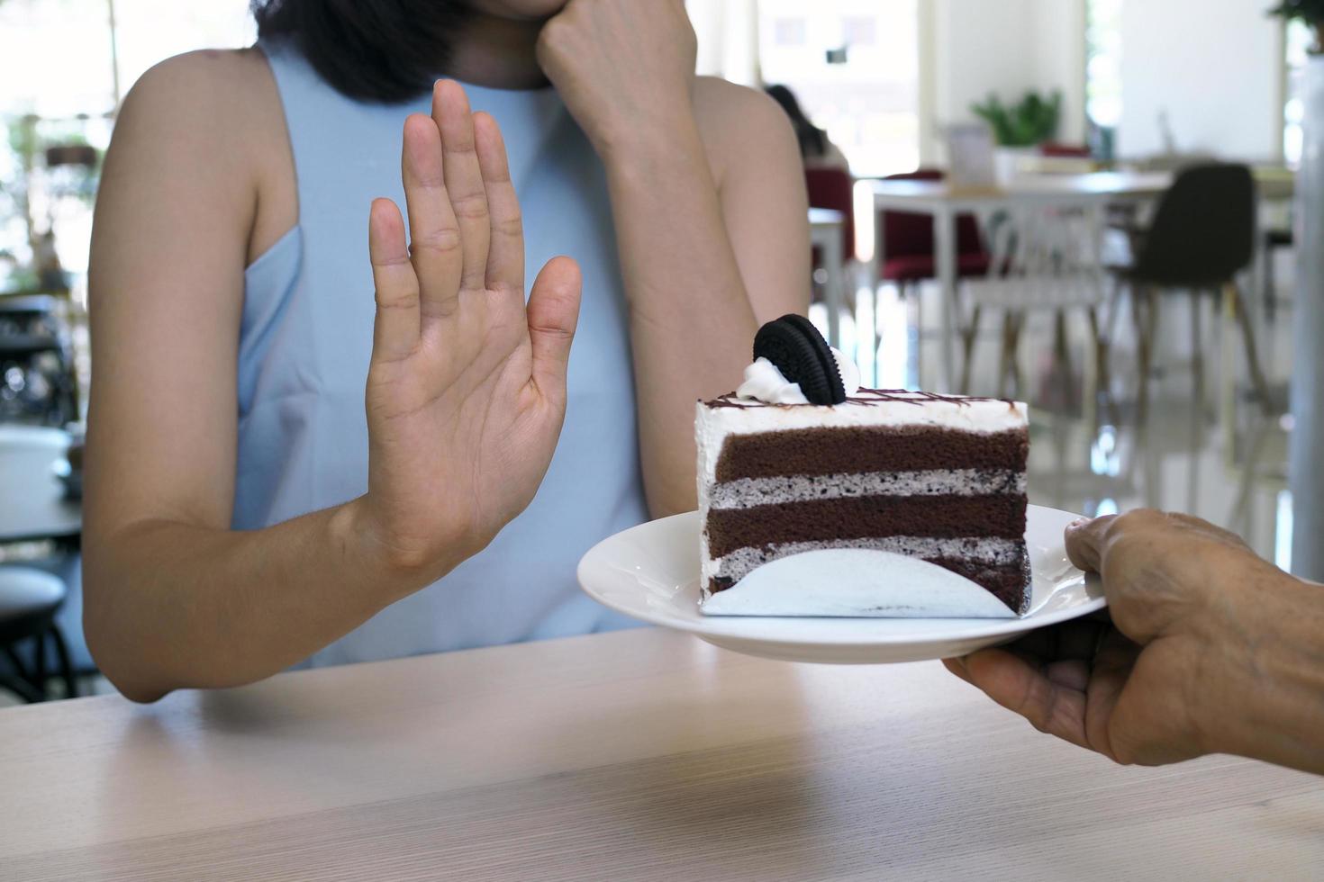 uma das moças do posto de saúde usou a mão para empurrar um prato de bolo de chocolate. recusar-se a comer alimentos que contenham gordura trans. foto