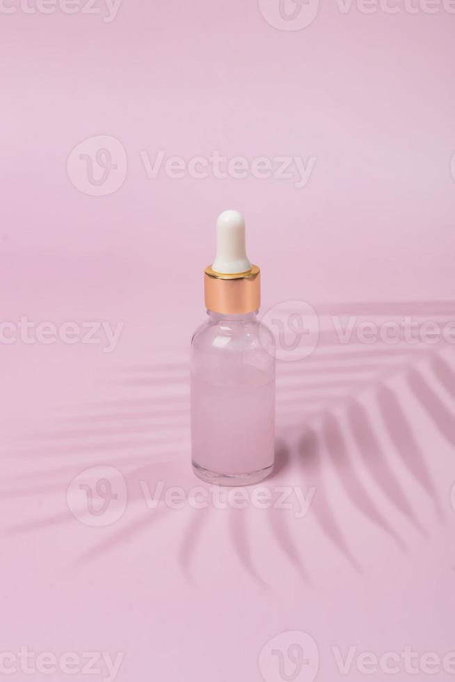 conta-gotas de frasco cosmético de vidro com óleo beuty ou soro para cuidados com a pele em fundo rosa. conceito de cuidado de pele natural. sombras duras de palmeira foto