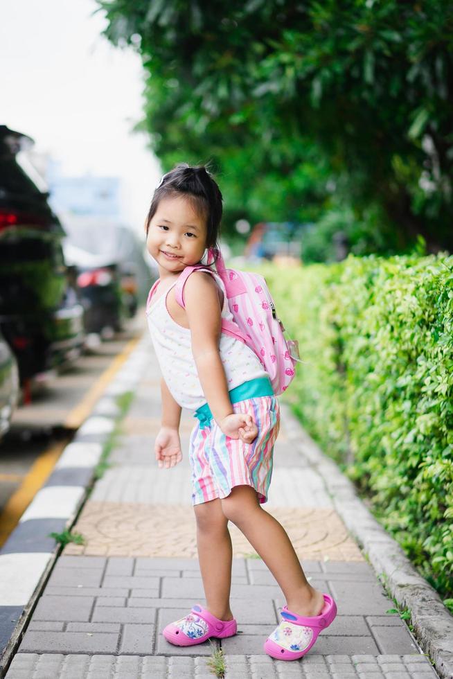 retrato de menina feliz com mochila em pé na calçada do parque foto