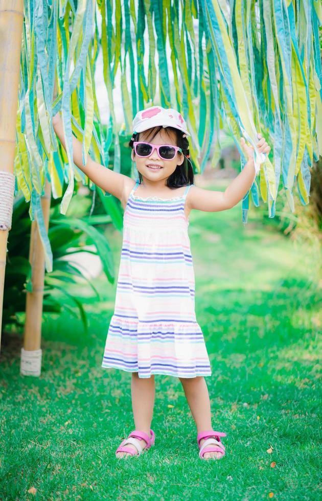 retrato de uma linda garotinha asiática usando óculos escuros e chapéu no parque foto