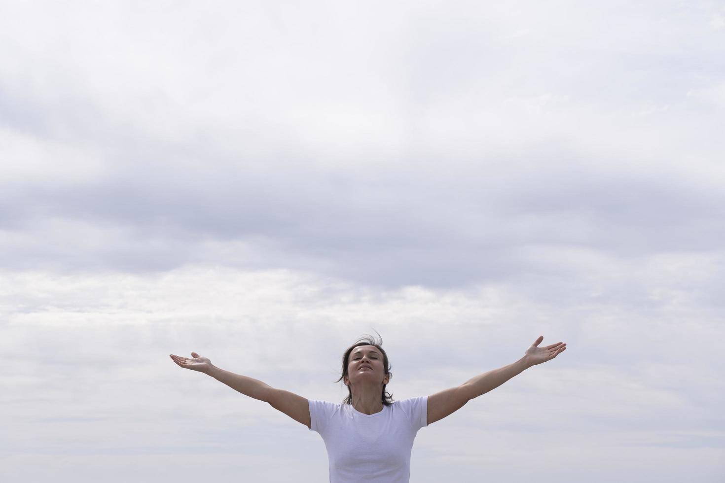 mulher na frente com camisa branca levantando os braços para o céu foto