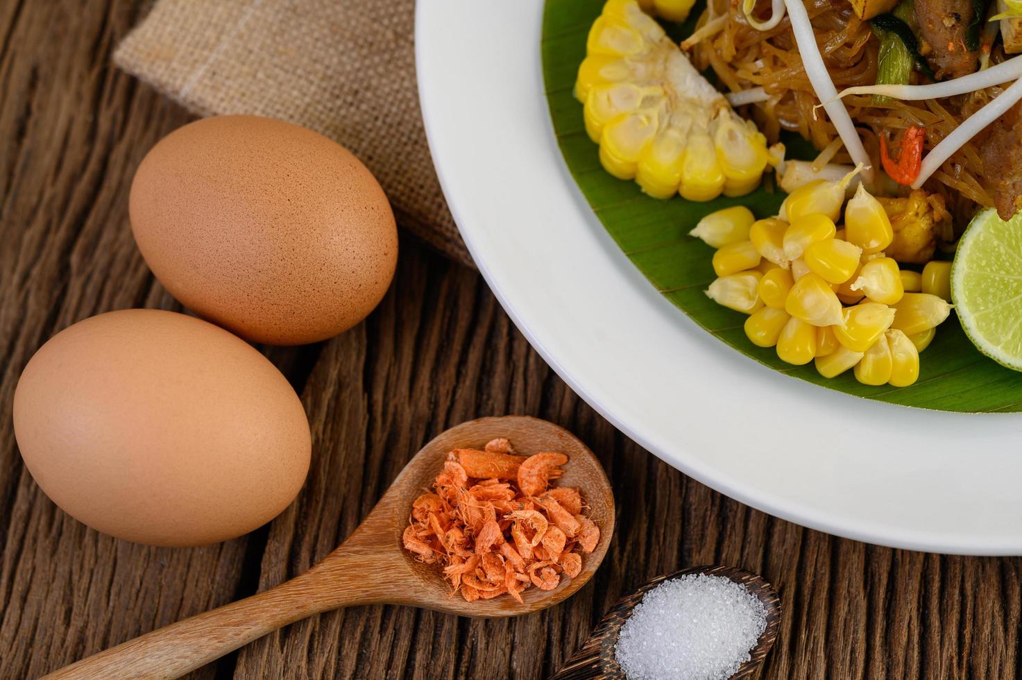 Pad thai com limão, ovos e temperos em uma mesa de madeira foto