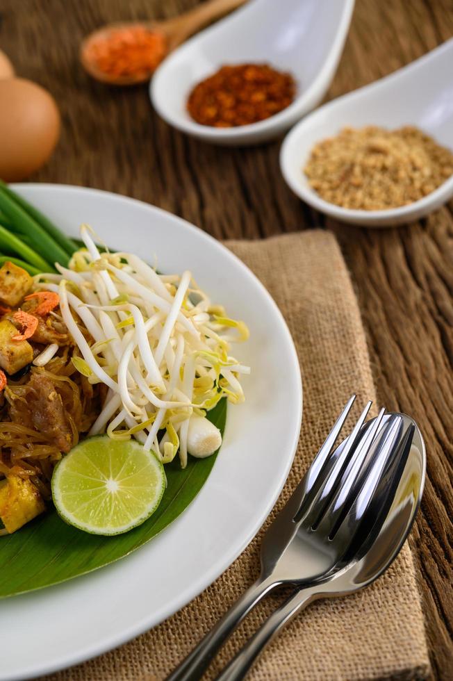 Pad thai com limão, ovos e temperos em uma mesa de madeira foto