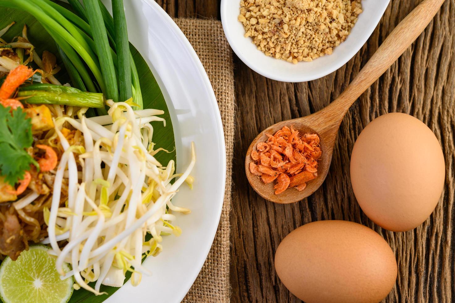 Pad thai com limão, ovos e temperos em uma mesa de madeira foto