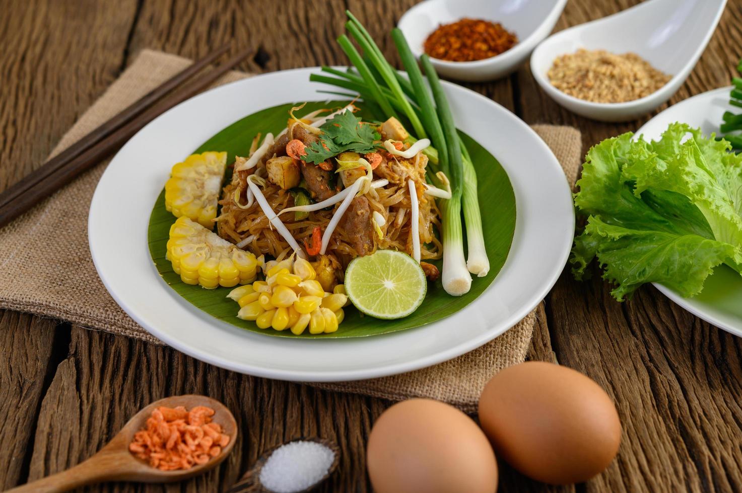 Pad thai com limão, ovos e temperos em uma mesa de madeira foto