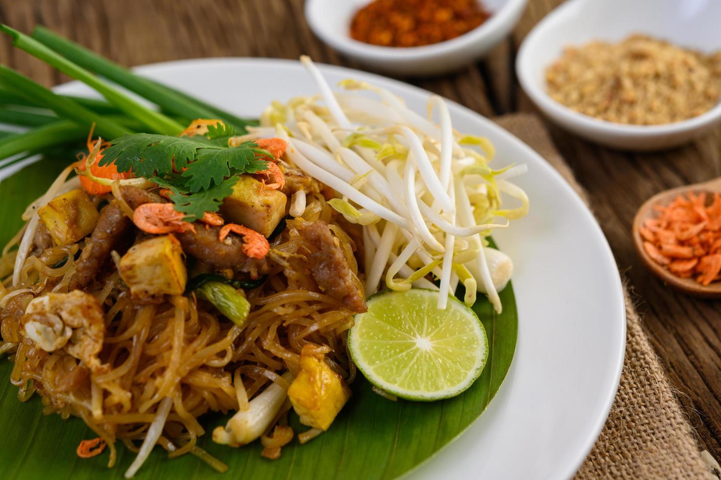 Pad thai com limão, ovos e temperos em uma mesa de madeira foto