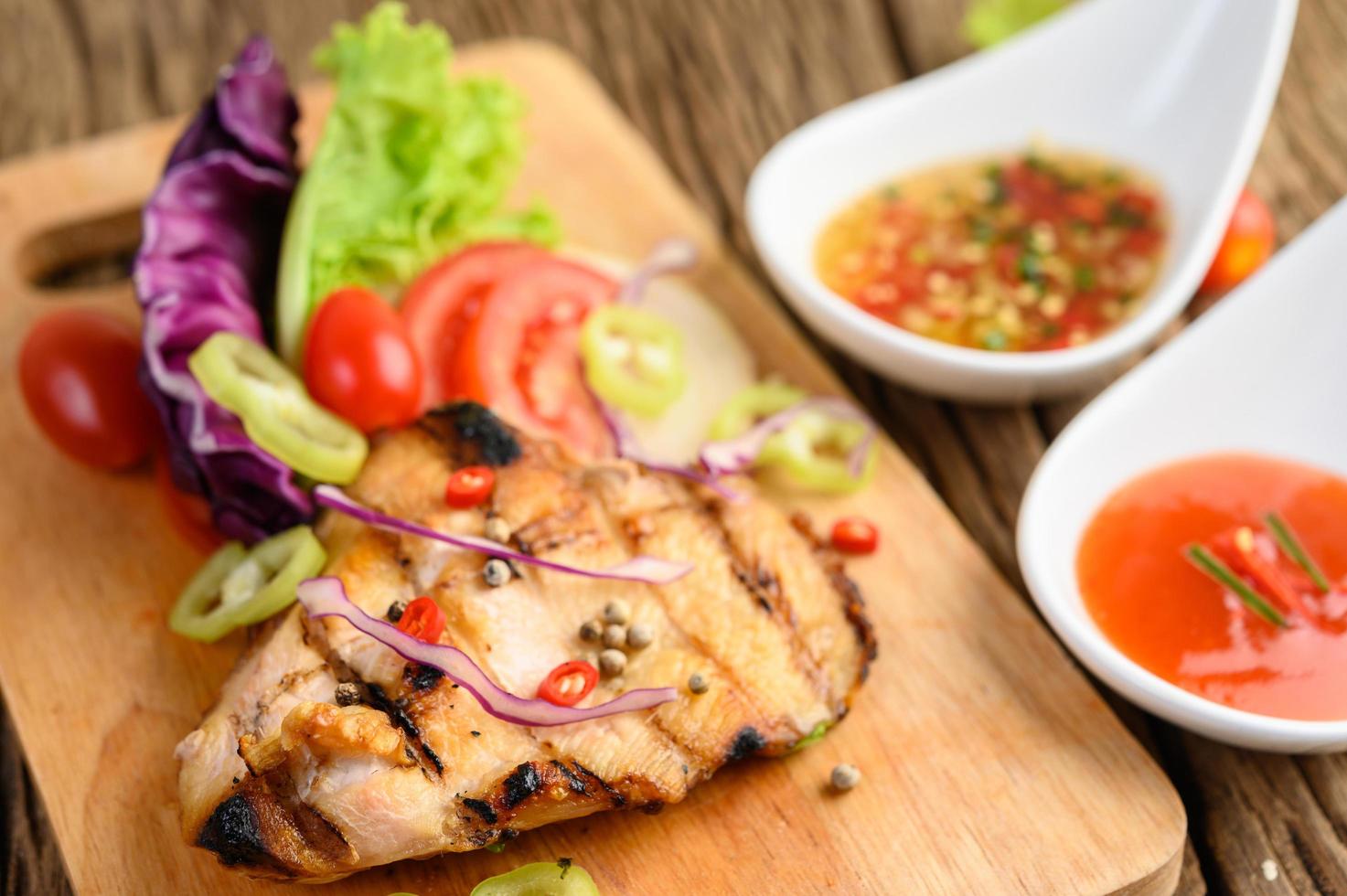 frango grelhado em uma tábua de madeira com salada foto