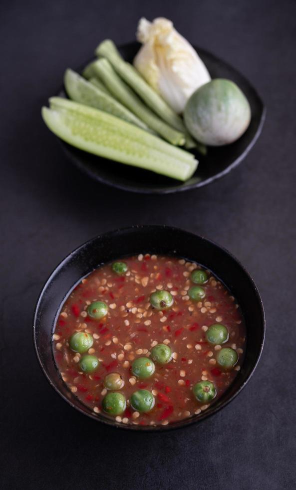 Molho de pasta de camarão em uma tigela preta com pepino, feijão e berinjela tailandesa foto