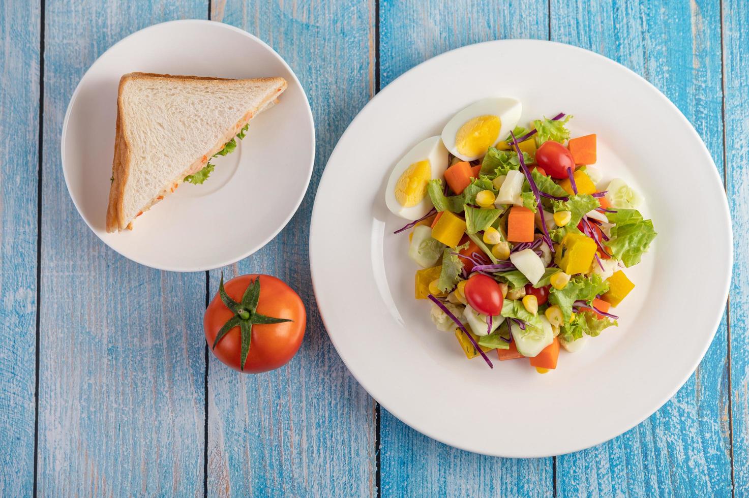 Salada fresca em um prato branco com um sanduíche e tomates foto