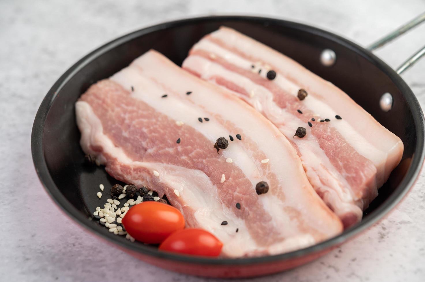 barriga de porco em uma panela com sementes de pimenta, tomate e especiarias foto