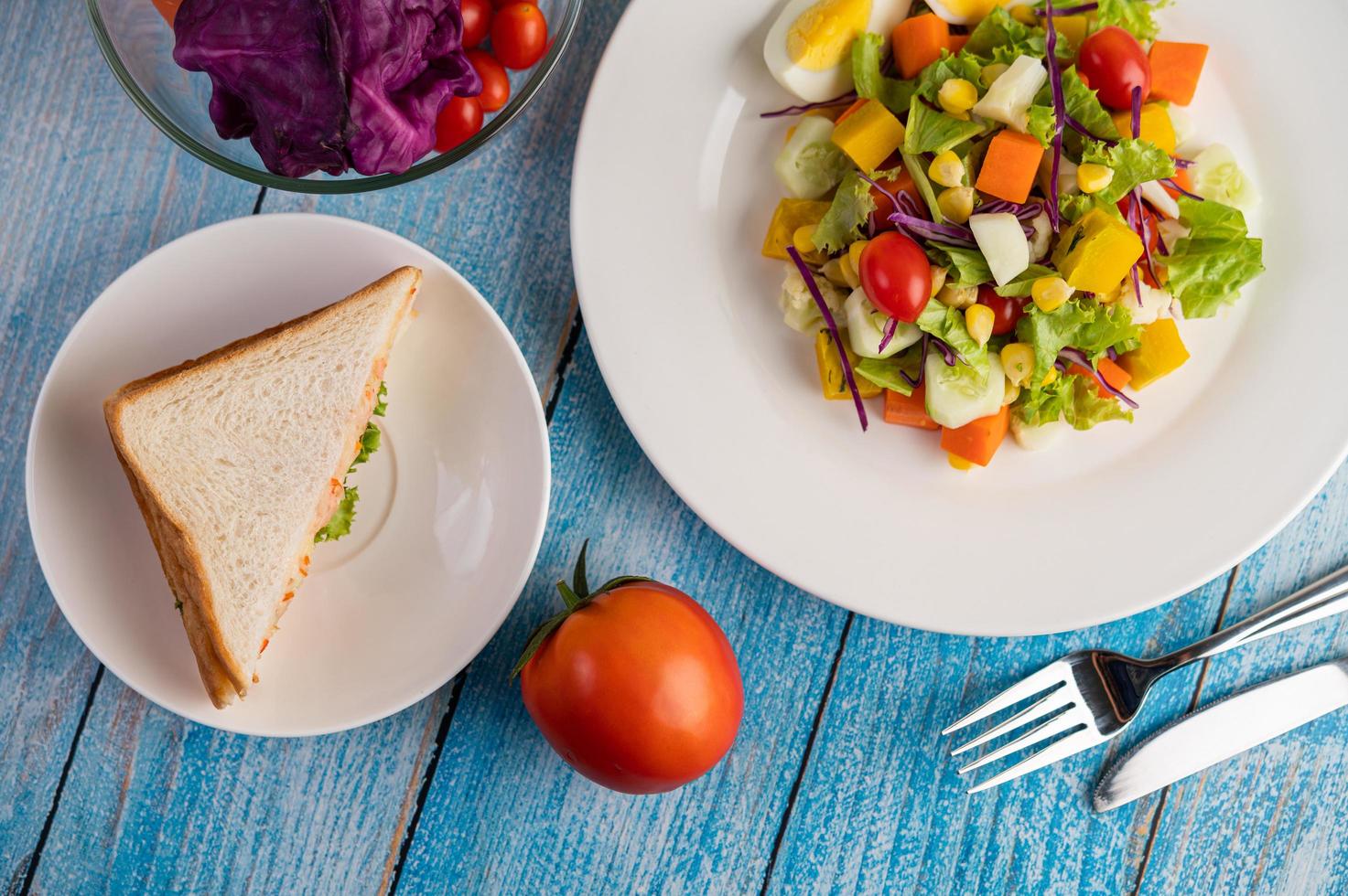 Salada fresca em um prato branco com um sanduíche e tomates foto