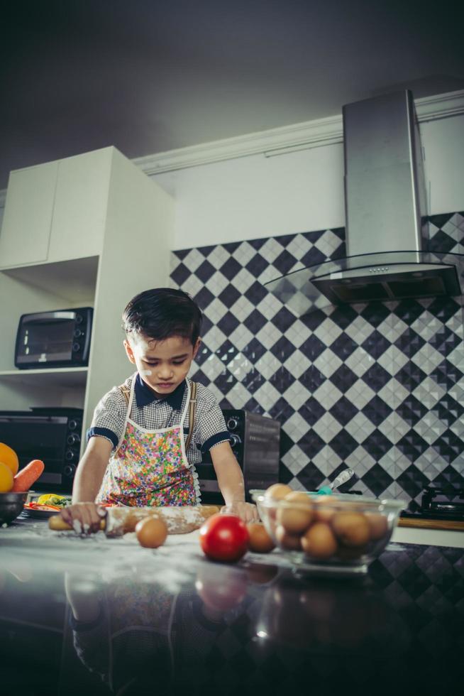 menino bonitinho aprendendo a cozinhar em pé na cozinha foto