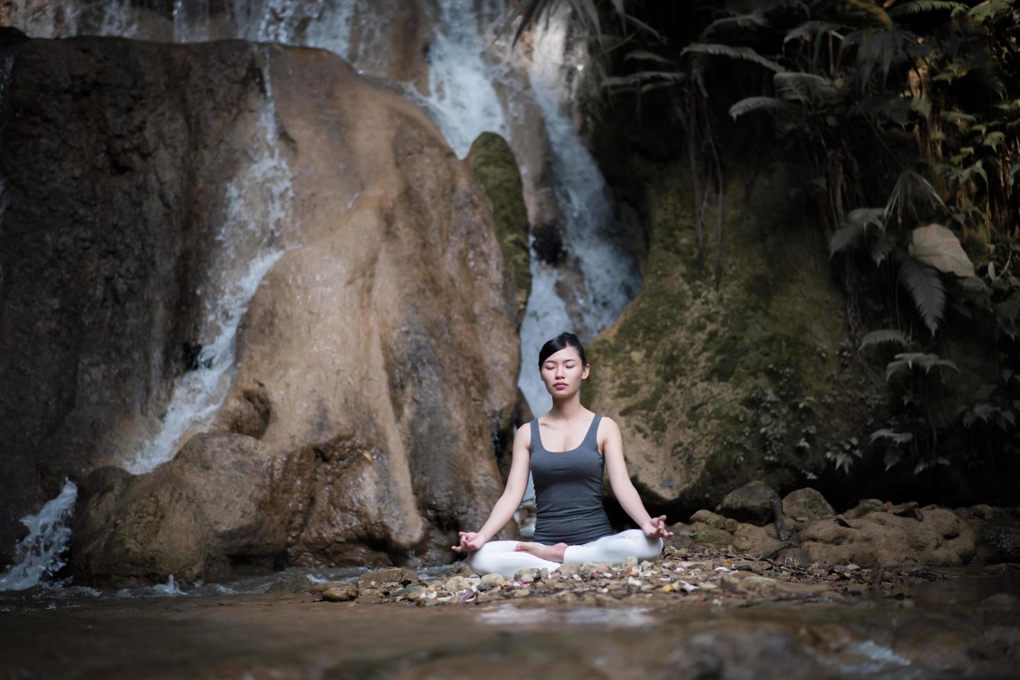 jovem em pose de ioga sentada perto de uma cachoeira foto