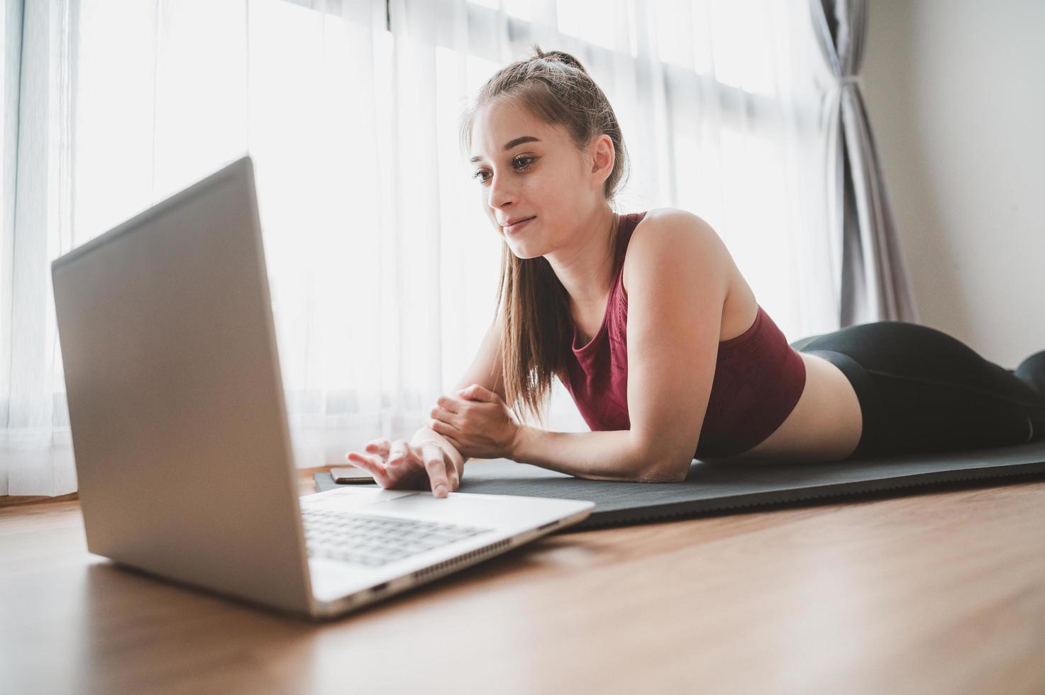 mulher em roupas esportivas deitada no chão usando laptop foto