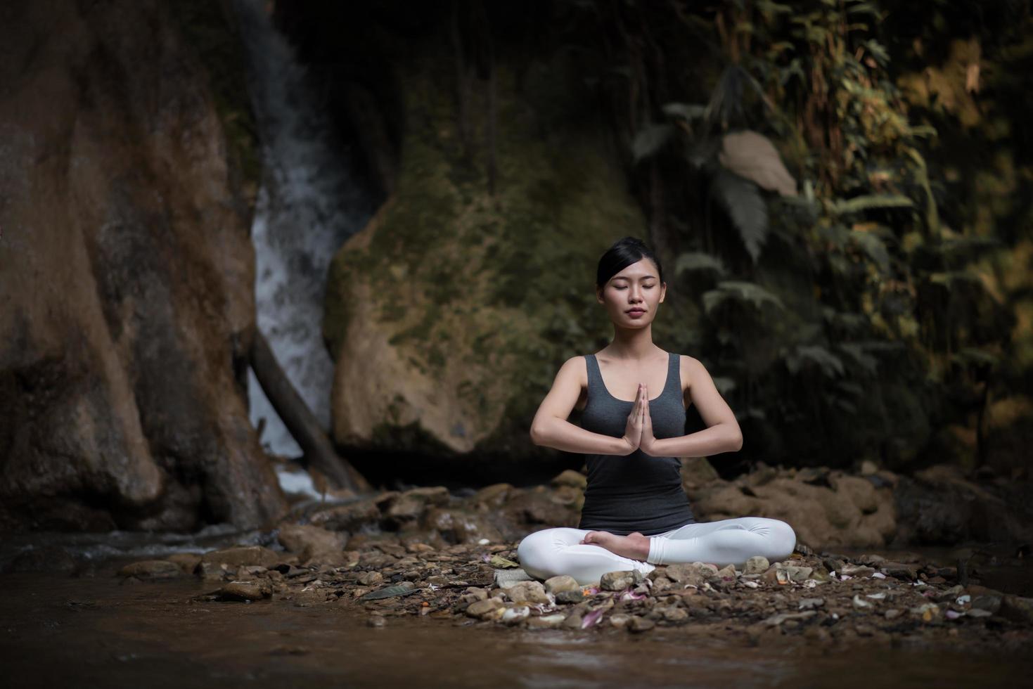 jovem em pose de ioga sentada perto de uma cachoeira foto