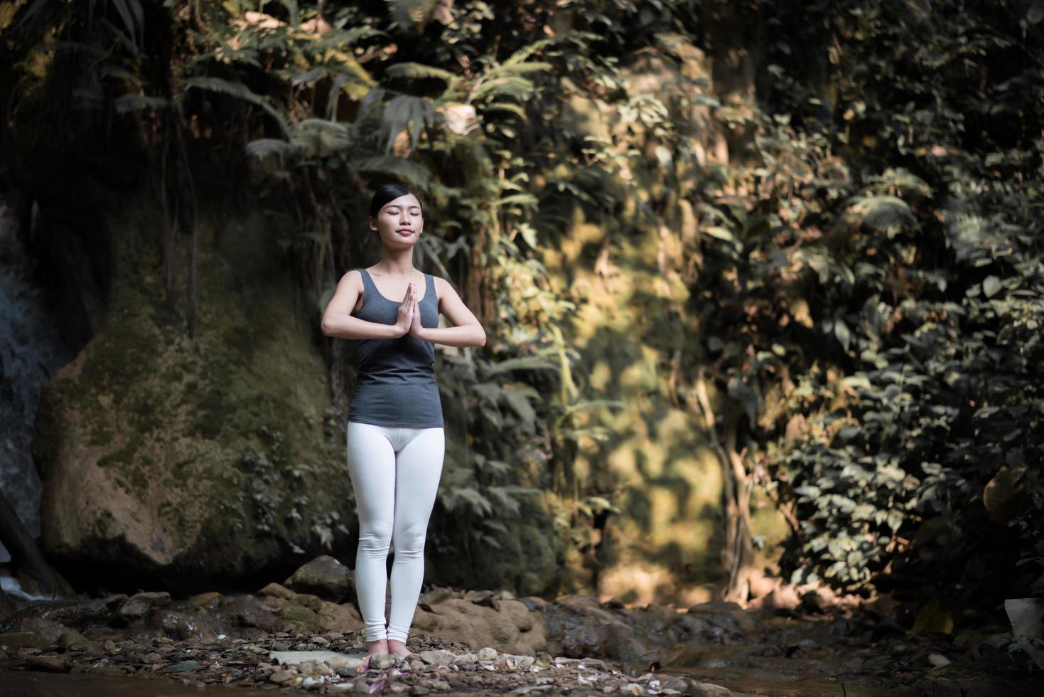 jovem fazendo pose de ioga perto de uma cachoeira foto