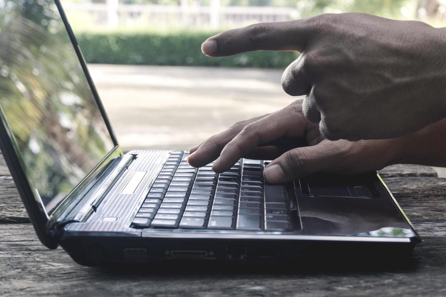 mão pessoa trabalhando apontando para a tela e usando em um computador laptop para freelance com teclado de entrada para trabalho de blogueiro online para computador preto em uma mesa de madeira em casa. foto