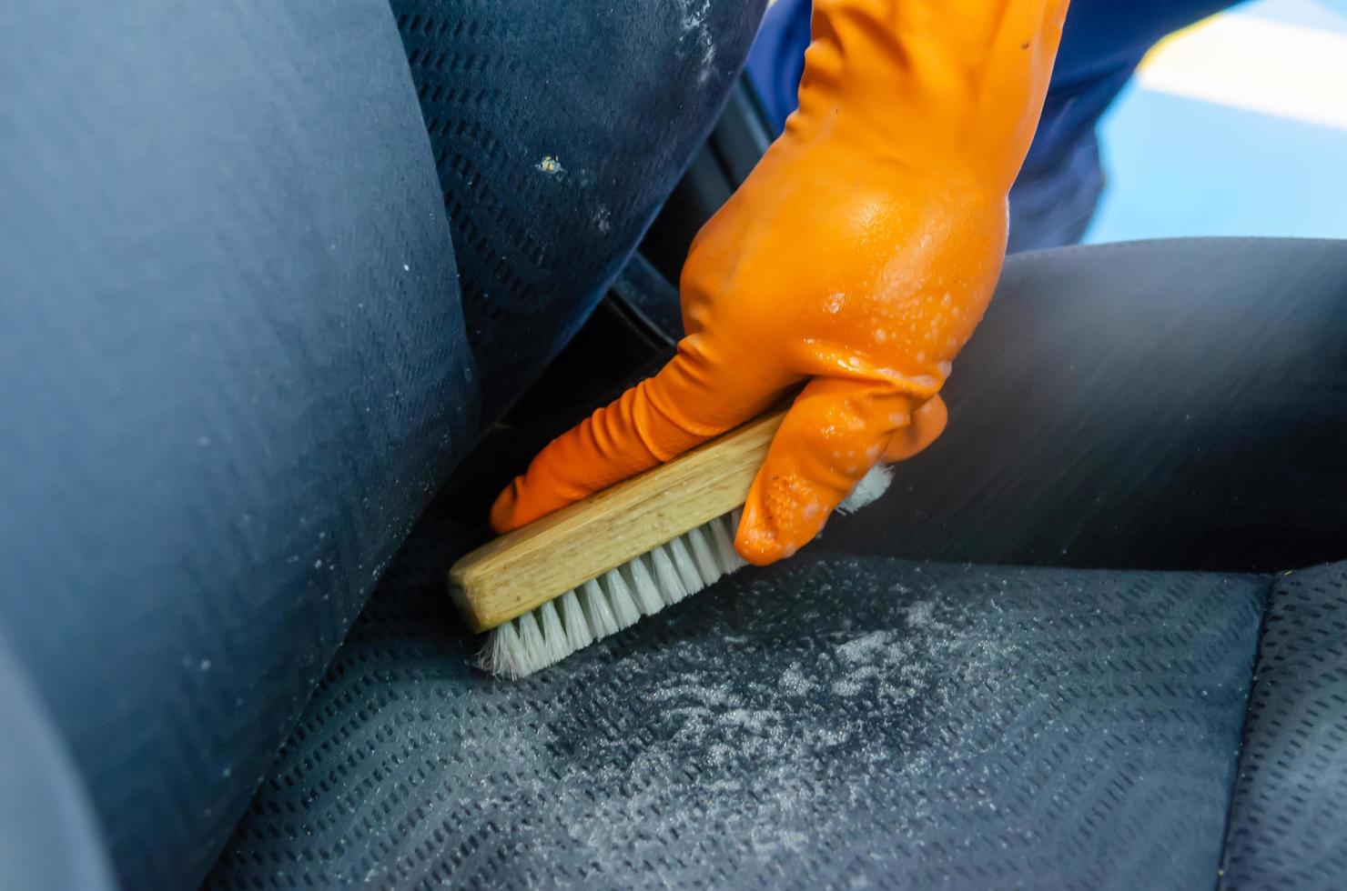 escovar o assento do carro limpo com luvas laranja foto