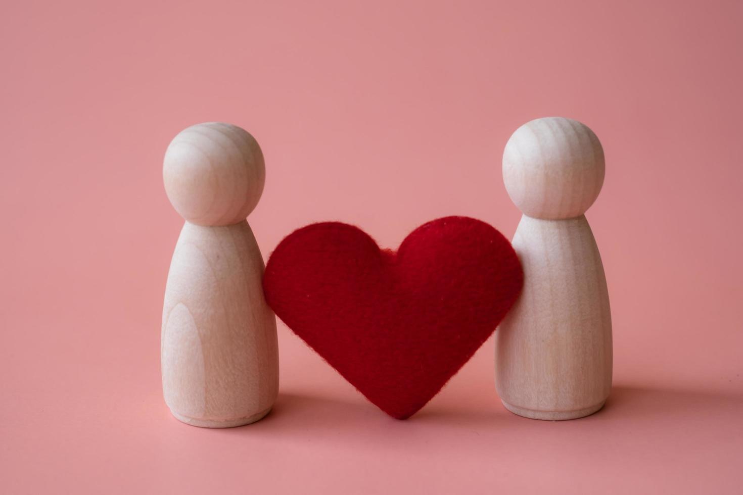 forma de coração vermelho entre estatuetas de madeira de mulher e mulher em fundo rosa. amo o conceito lgbtq. minorias sexuais e conceito de comunidades foto