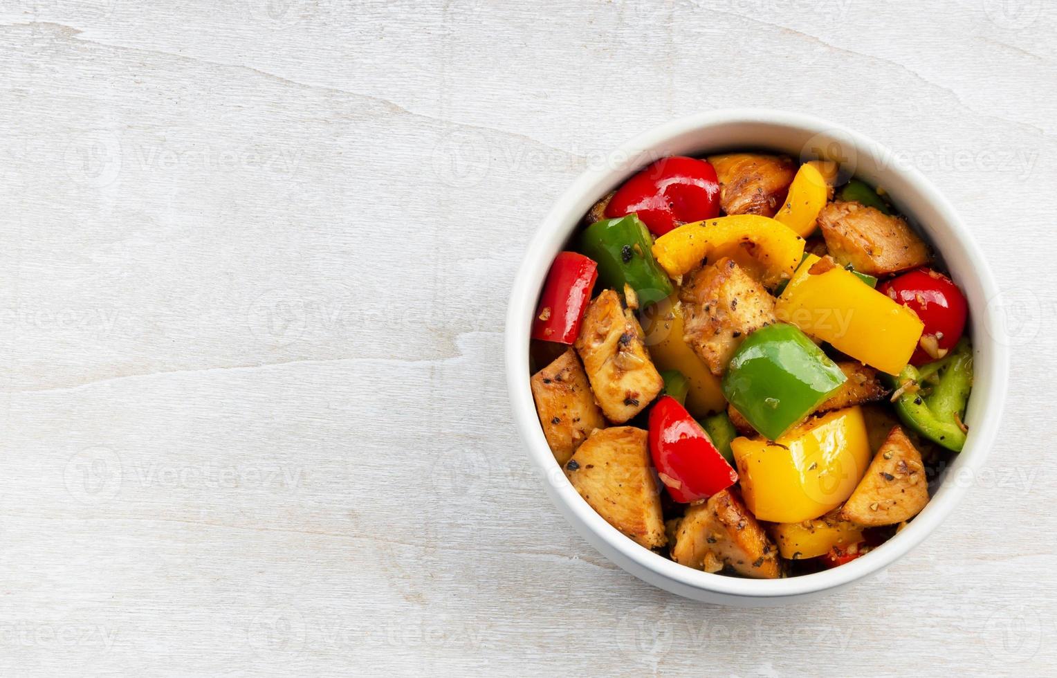 comida saudável mexa frango frito adicione pimentão na tigela na mesa de madeira. foto