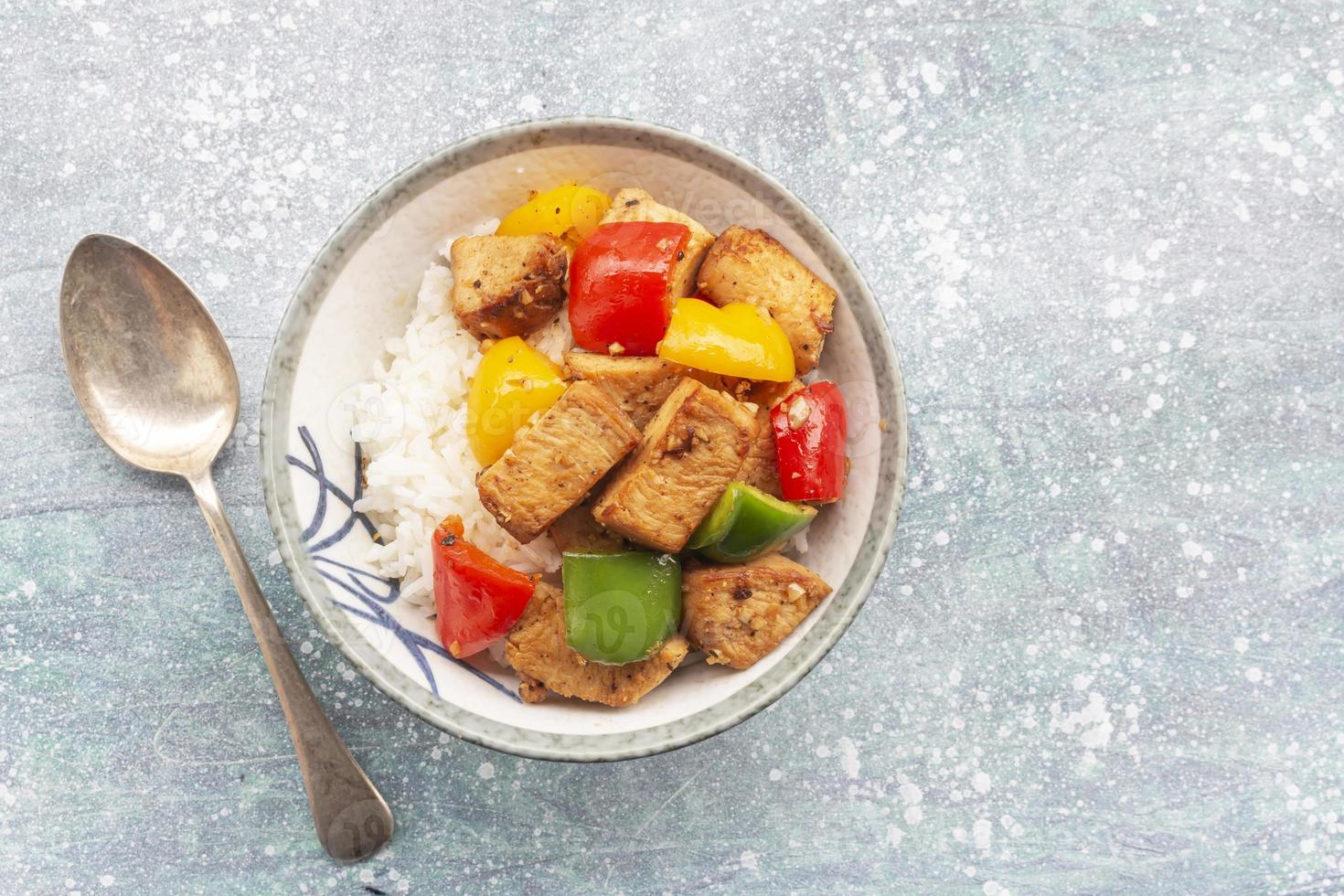 comida saudável mexer frango frito adicionar pimentão tem arroz na tigela na mesa de madeira azul. foto