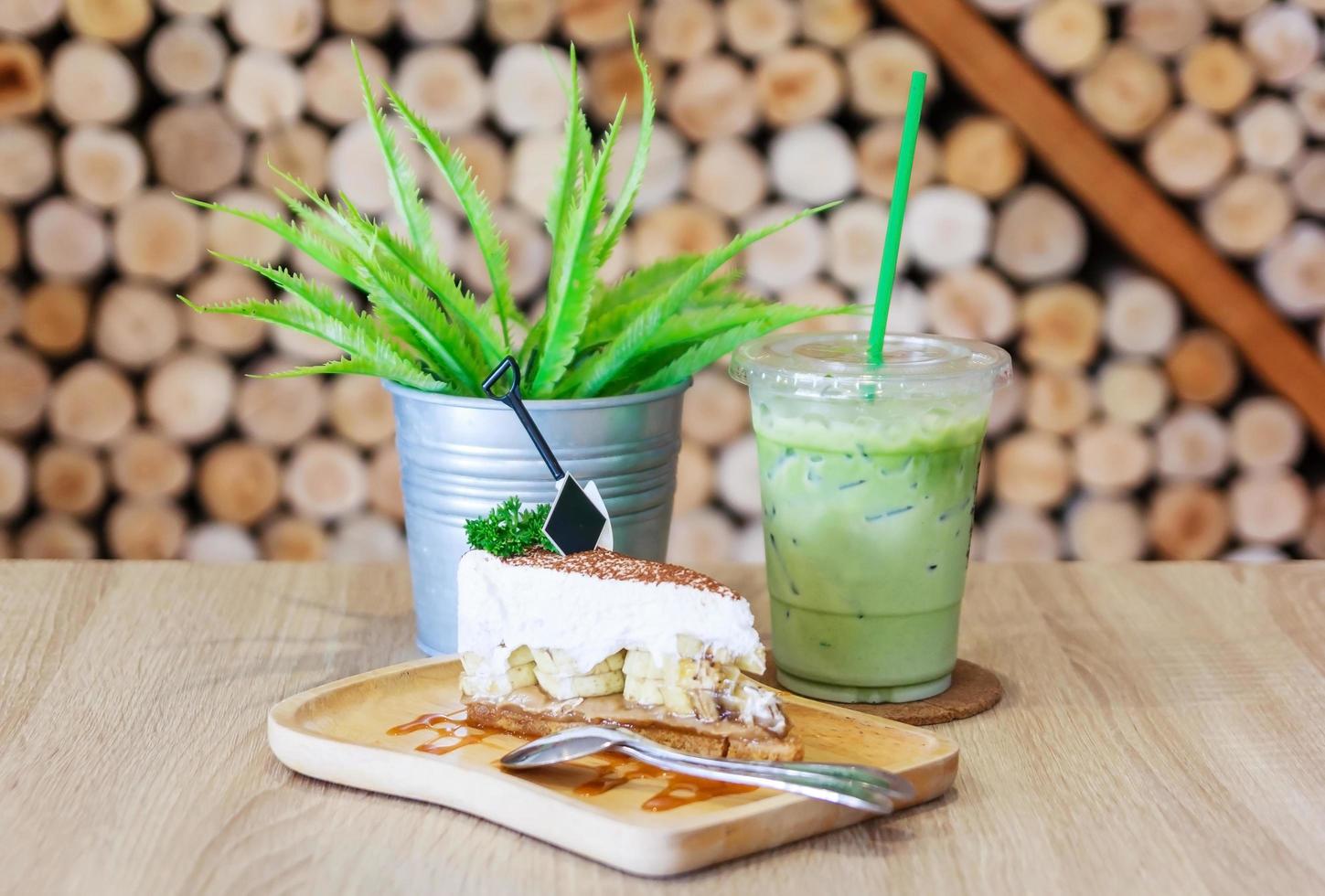 Feche acima da bebida de chá verde e bolo de banoffee com cobertura de caramelo em um prato branco no fundo da mesa de madeira foto