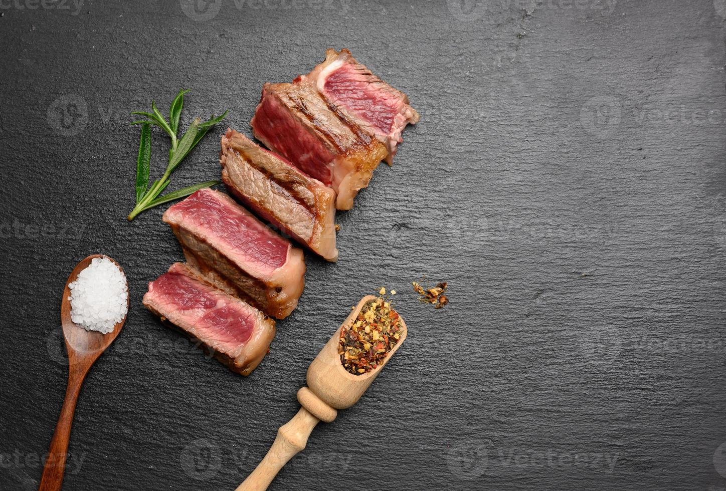 filé de carne frita fatiado New York striploin em um fundo preto com especiarias, grau de cozimento raro foto