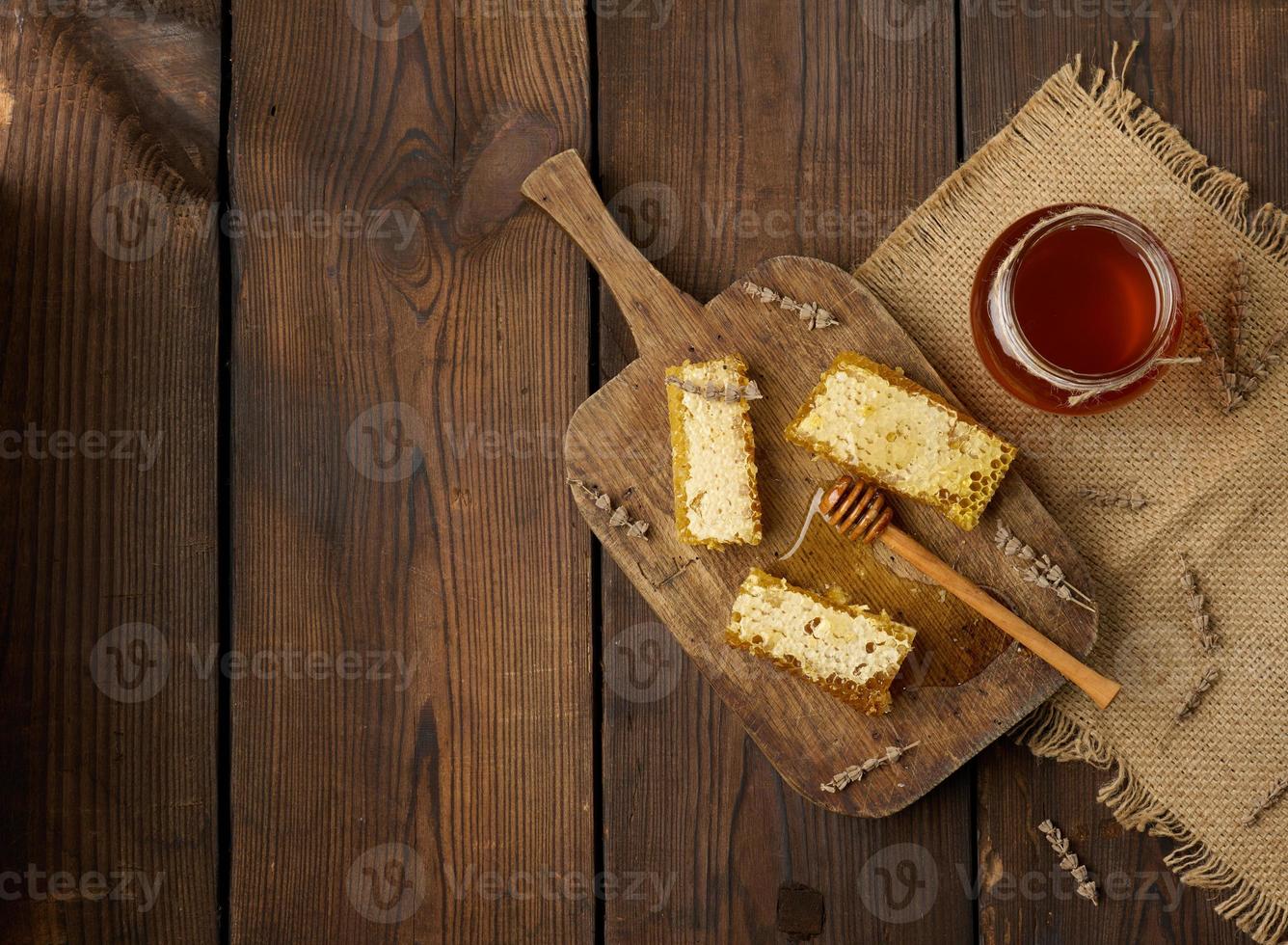 favo de mel de abelha de cera com mel na placa de madeira e colher de pau, mesa marrom, vista superior foto