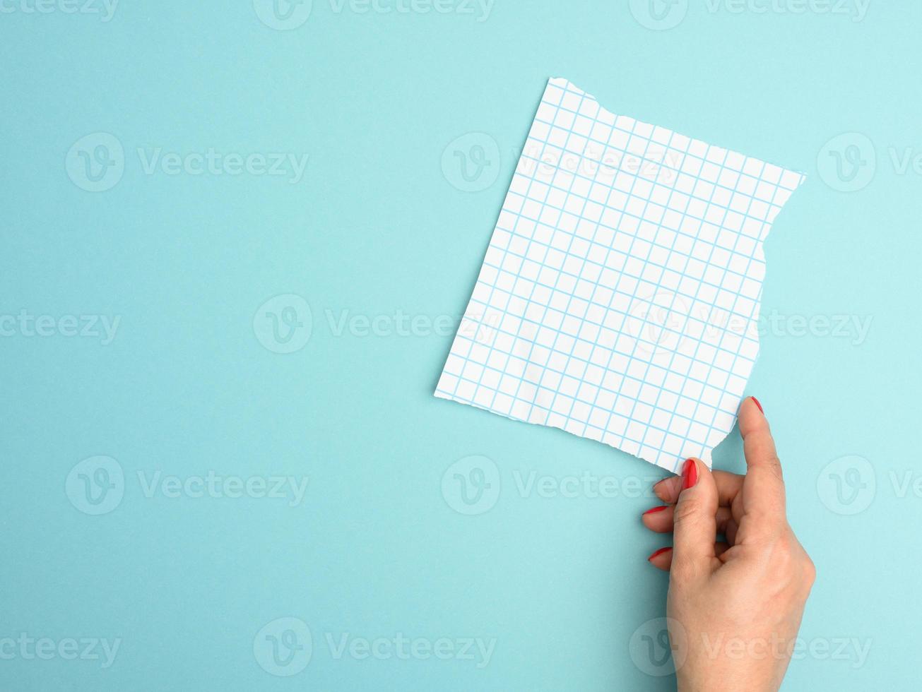 mão feminina segurando uma folha de papel em branco rasgada em uma gaiola em um fundo azul foto