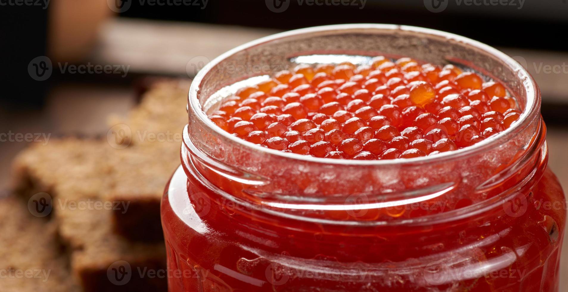 frasco de vidro cheio com caviar vermelho em uma mesa de madeira marrom, vista superior foto