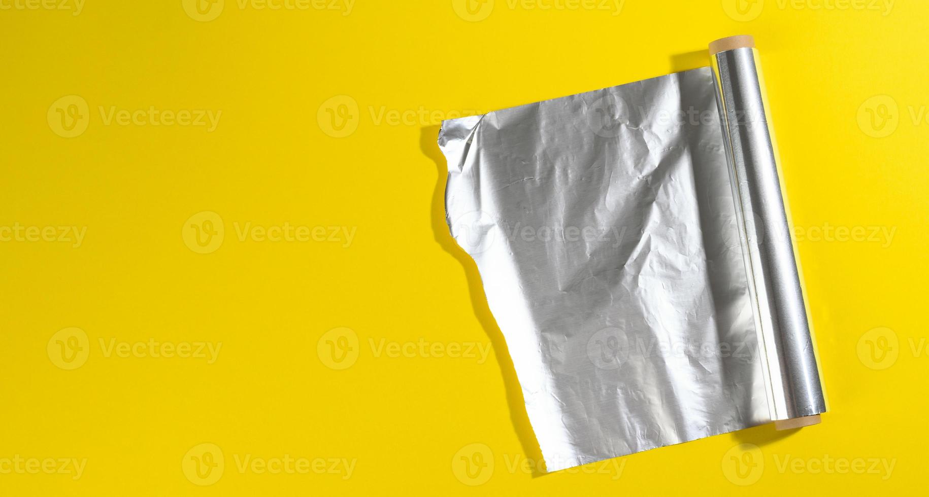 rolo de papel alumínio torcido para embalar alimentos em fundo amarelo foto