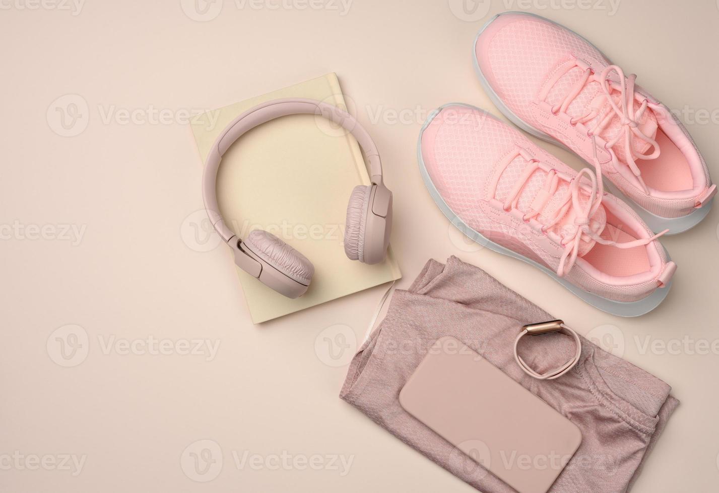 par de tênis rosa, fones de ouvido sem fio, um smartphone e um relógio inteligente em um fundo rosa foto