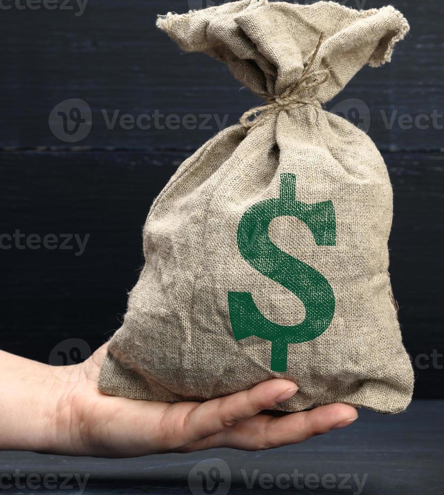 mão segura um saco de lona cheio de dinheiro com um ícone de dólar americano sobre um fundo azul. conceito de planejamento orçamentário foto