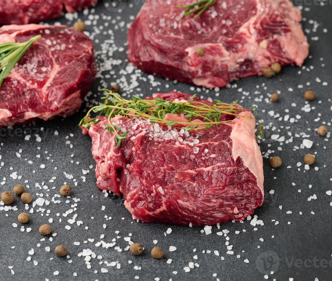 pedaço cru de ribeye de carne com alecrim, tomilho em uma mesa preta foto