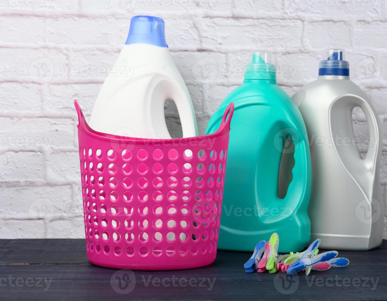 cesto de roupa suja rosa vazio e garrafas de plástico com detergente líquido foto