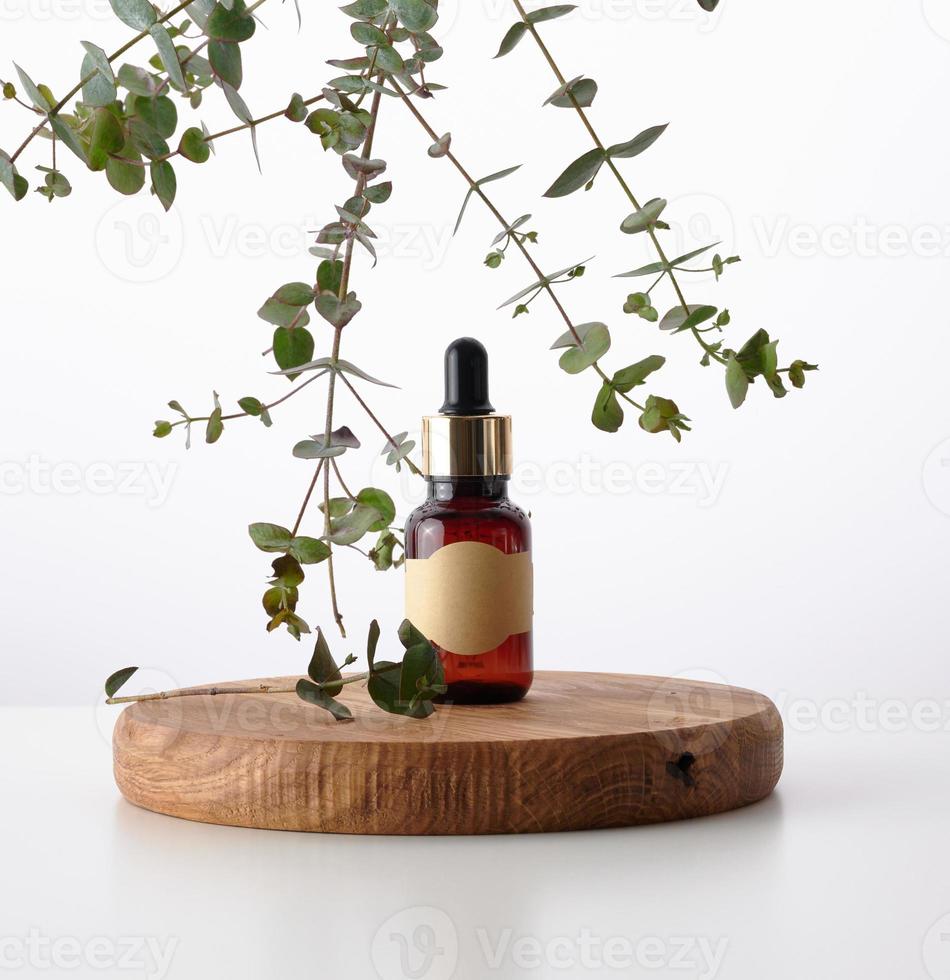 garrafa de vidro marrom com uma pipeta em um pódio de madeira e um ramo de eucalipto. publicidade e promoção de produtos cosméticos foto