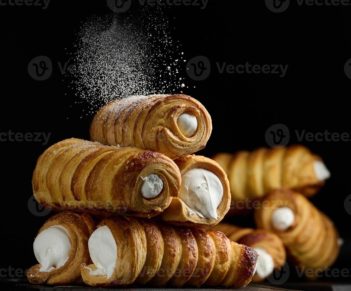 túbulos assados cheios de creme de clara de ovo batido em uma placa de cozinha de madeira preta foto